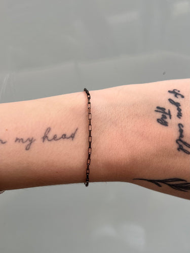 Bracelet on a wrist with tattoos against a neutral background